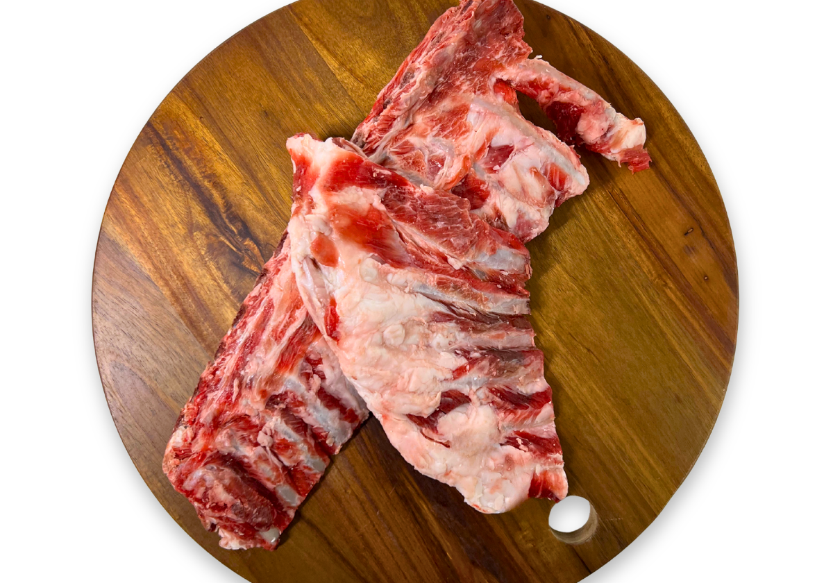 Two raw goat rib sections for raw feeding to dogs with visible bone and marbling, arranged on a round wooden cutting board against a plain white background.