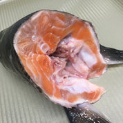 A raw salmon fillet cut open, showing the pink-orange flesh and white fat, placed on a light gray ribbed surface.